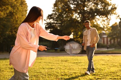 Photo of Young woman and man playing badminton in park on sunny day, selective focus