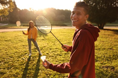 Young man and woman playing badminton in park on sunny day, selective focus