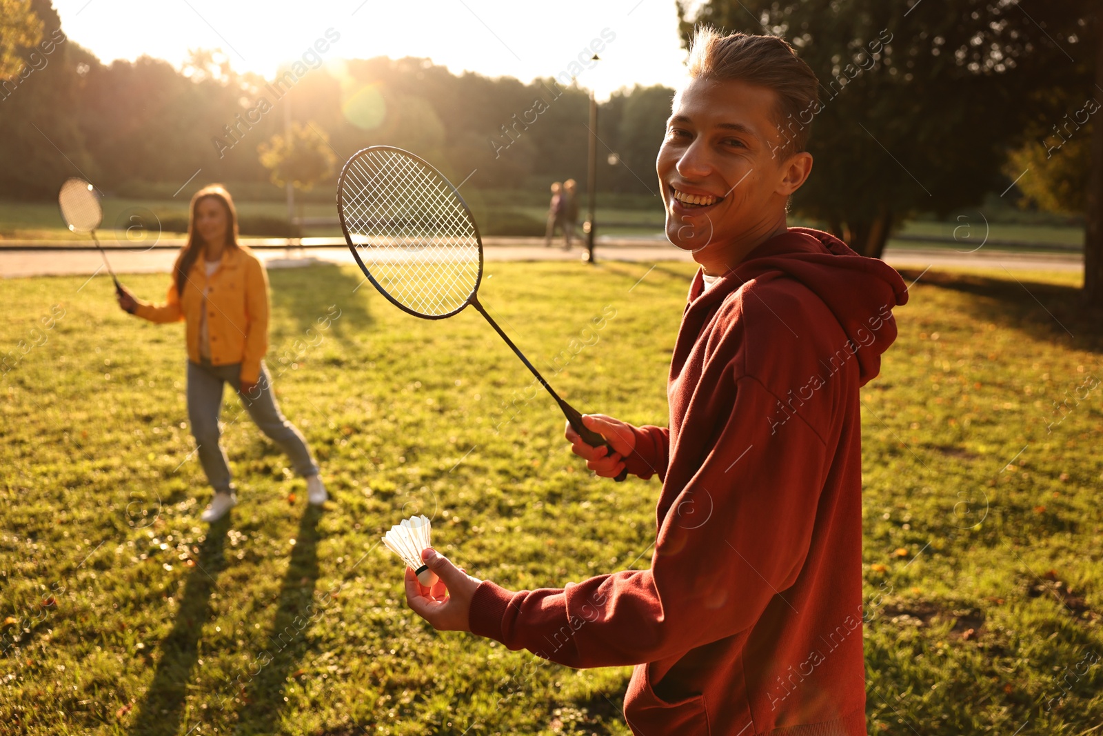 Photo of Young man and woman playing badminton in park on sunny day, selective focus