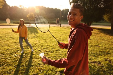 Photo of Young man and woman playing badminton in park on sunny day, selective focus