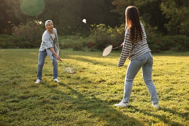 Young man and woman playing badminton in park on sunny day, selective focus