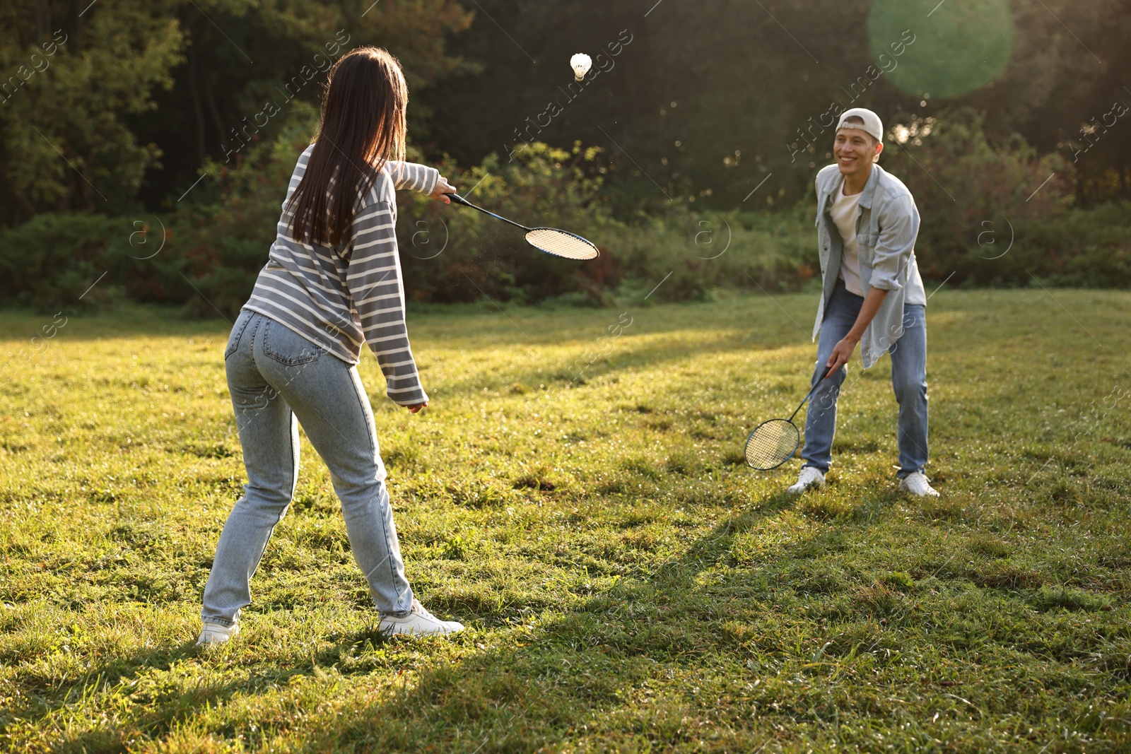 Photo of Young man and woman playing badminton in park on sunny day, selective focus