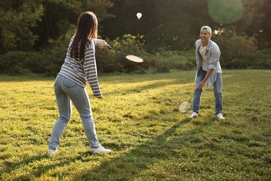 Young man and woman playing badminton in park on sunny day, selective focus