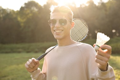 Happy young man with badminton racket and shuttlecock in park on sunny day