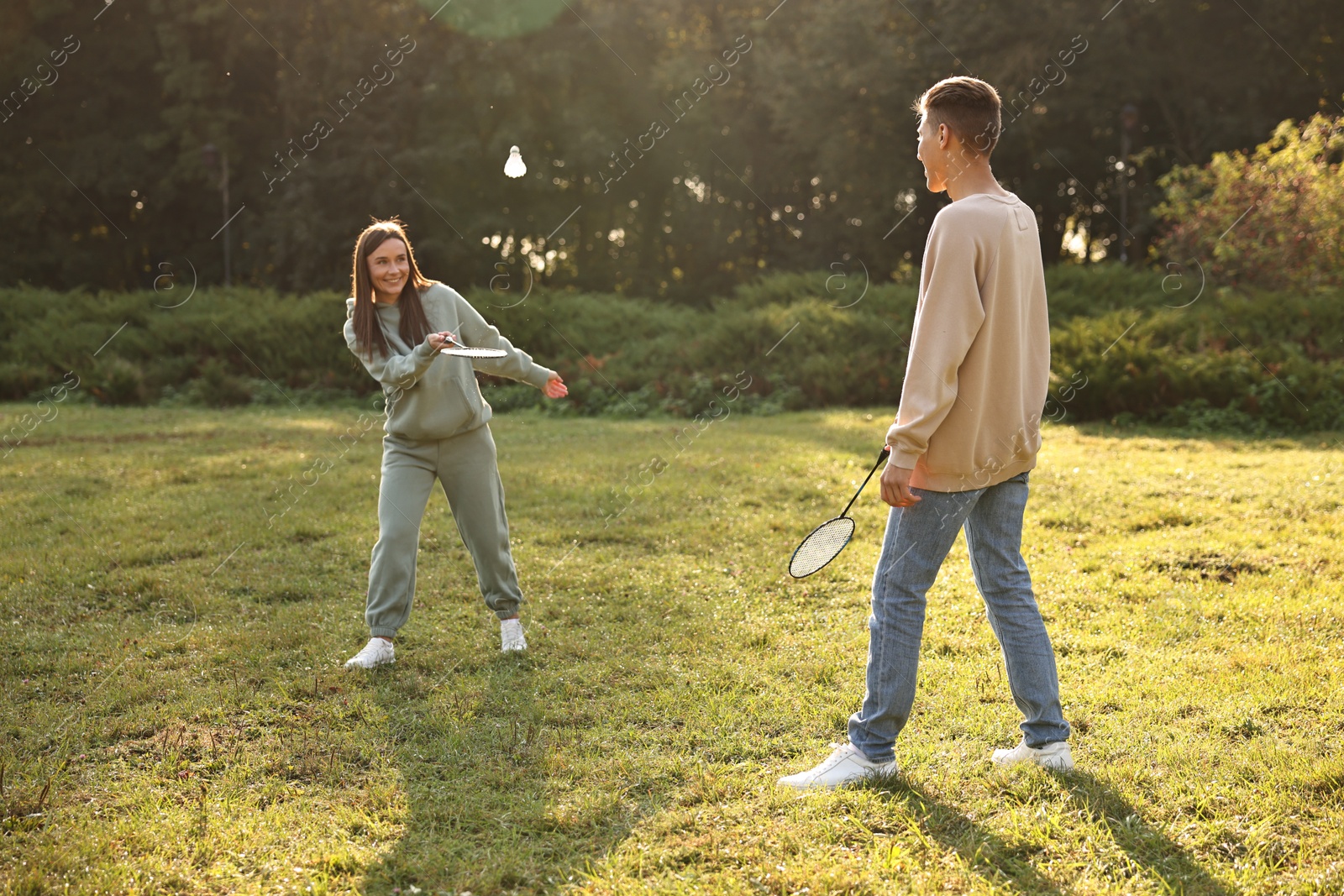 Photo of Young woman and man playing badminton in park on sunny day, selective focus