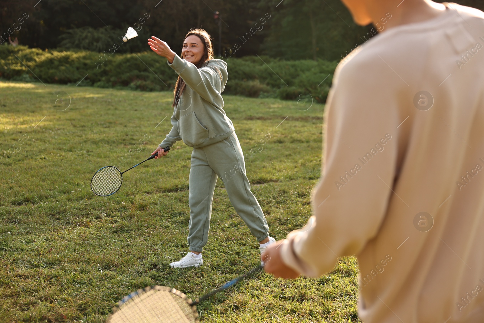 Photo of Young woman and man playing badminton in park on sunny day, selective focus