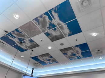 Photo of White ceiling with lighting and pictures of blue sky indoors, low angle view