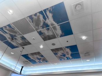 Photo of White ceiling with lighting and pictures of blue sky indoors, low angle view