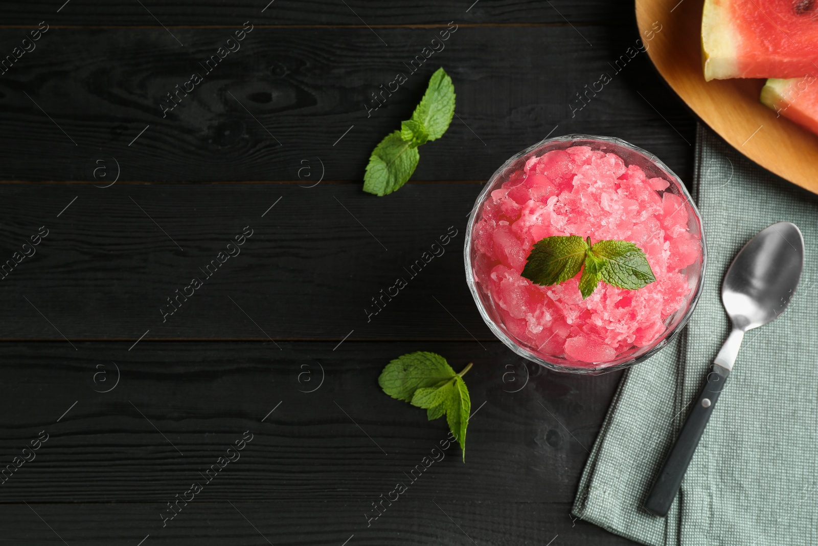 Photo of Tasty watermelon sorbet with mint in glass dessert bowl and spoon on black wooden table, flat lay. Space for text