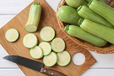 Photo of Fresh zucchinis and knife on white wooden table, flat lay