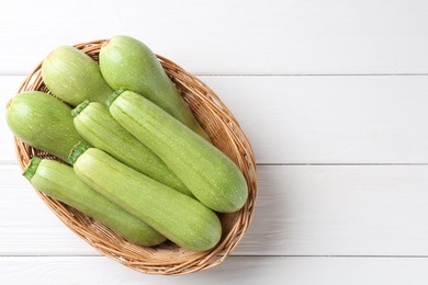 Photo of Fresh zucchinis in wicker basket on white wooden table, top view. Space for text