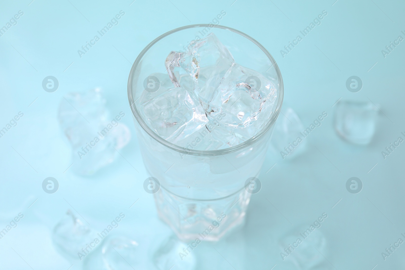 Photo of Refreshing water in glass with ice cubes on light blue background, closeup