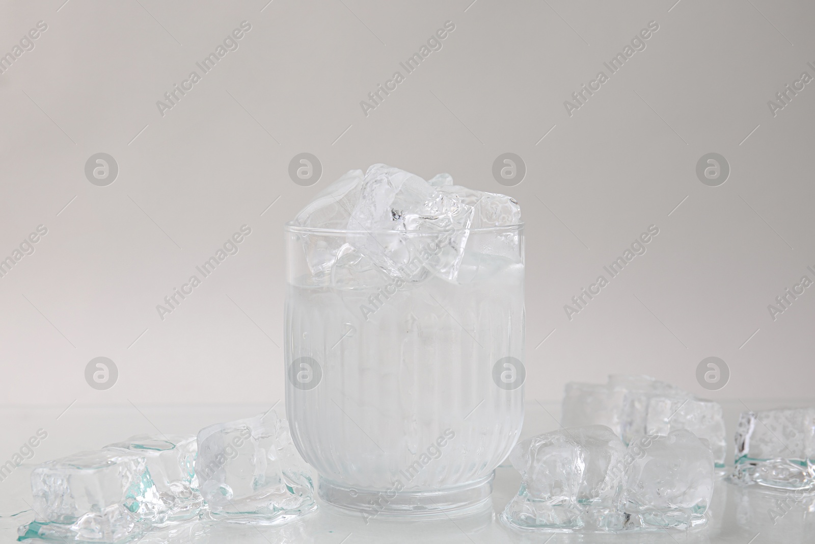 Photo of Refreshing water in glass with ice cubes on light background