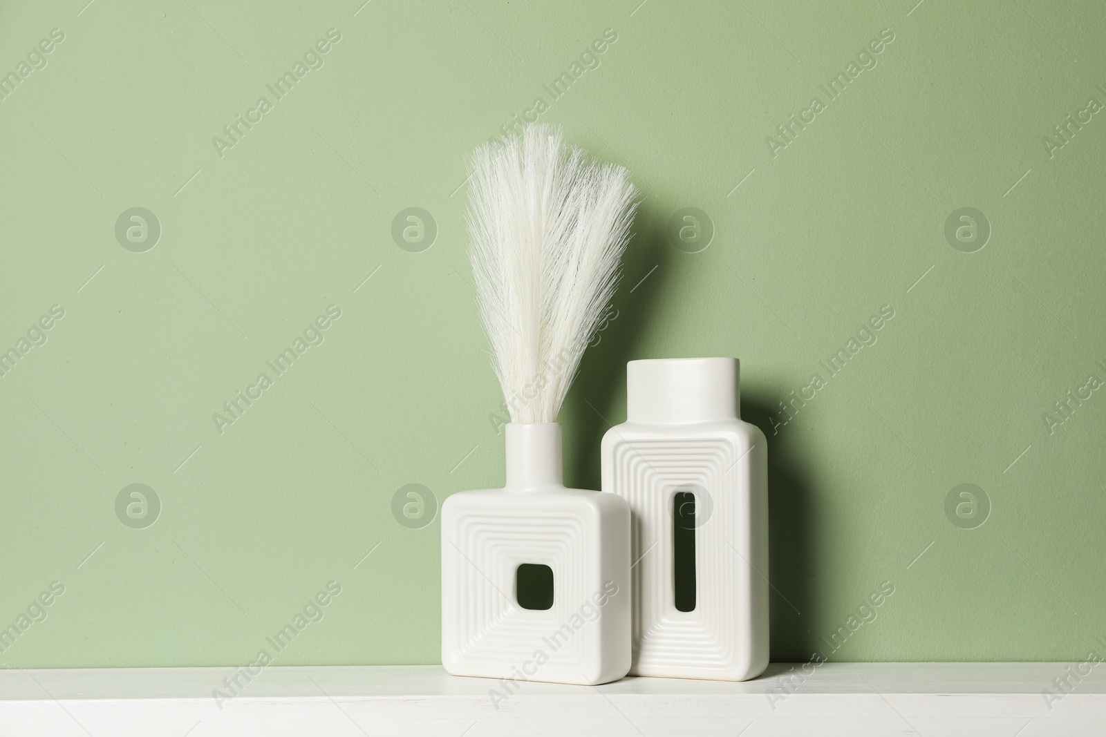 Photo of Beautiful decorative plants and vases on white shelf near green wall indoors, space for text