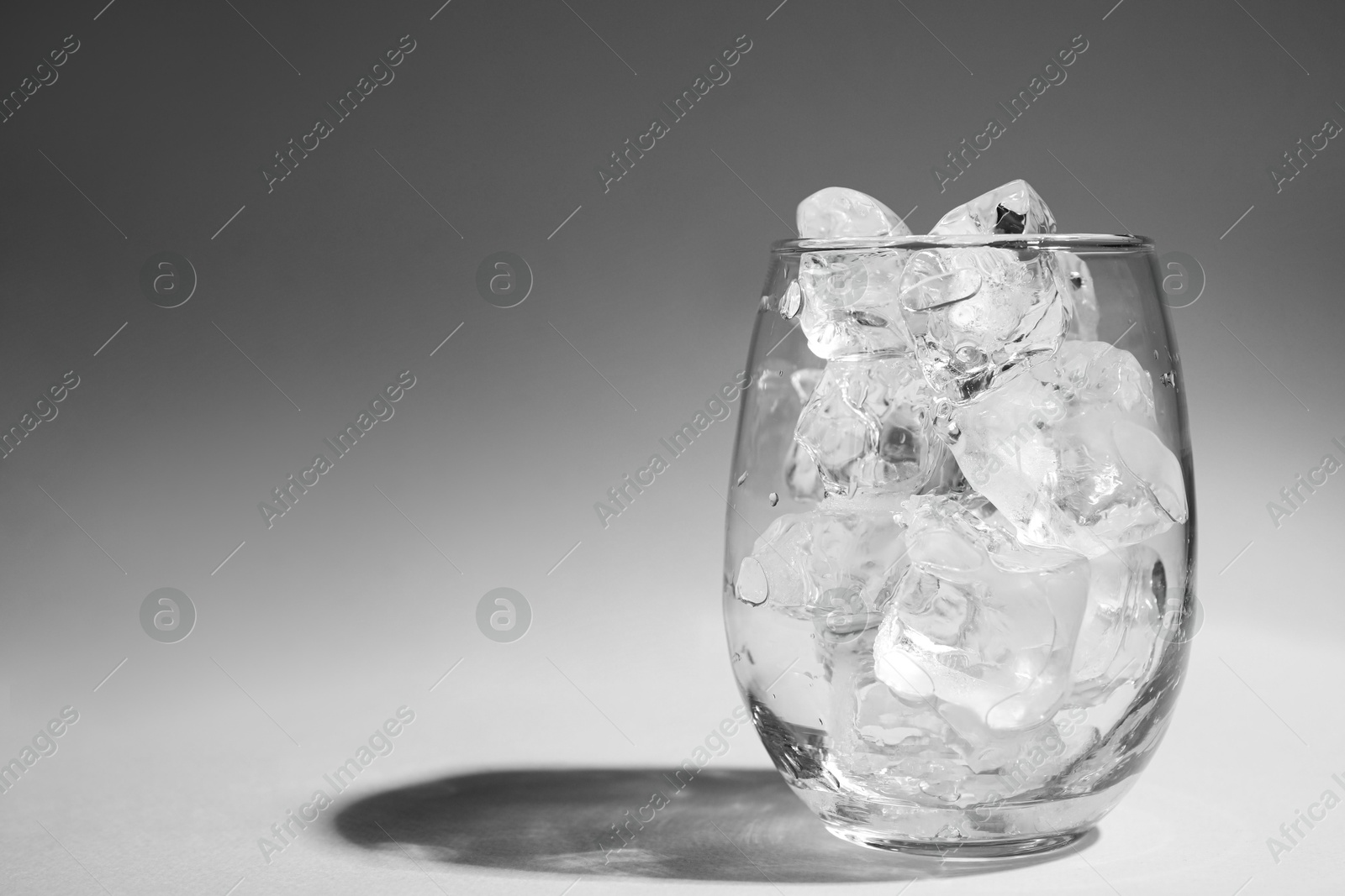 Photo of One glass with ice for refreshing drink on grey background. Space for text