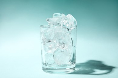 One glass with ice for refreshing drink on turquoise background, closeup