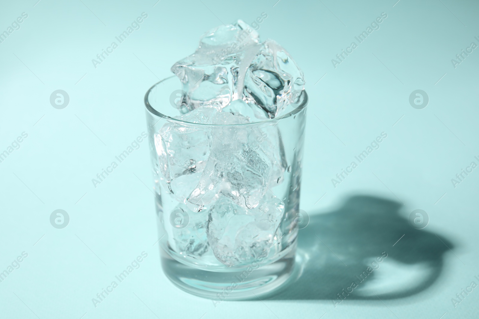 Photo of One glass with ice for refreshing drink on turquoise background, closeup