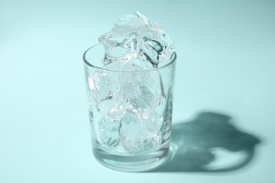 One glass with ice for refreshing drink on turquoise background, closeup