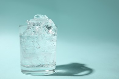 Photo of Refreshing water with ice in glass on turquoise background. Space for text