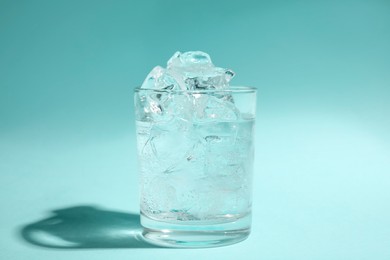 Photo of Refreshing water with ice in glass on turquoise background