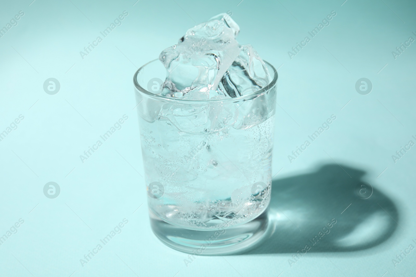 Photo of Refreshing water with ice in glass on turquoise background, closeup