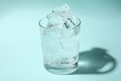 Photo of Refreshing water with ice in glass on turquoise background, closeup