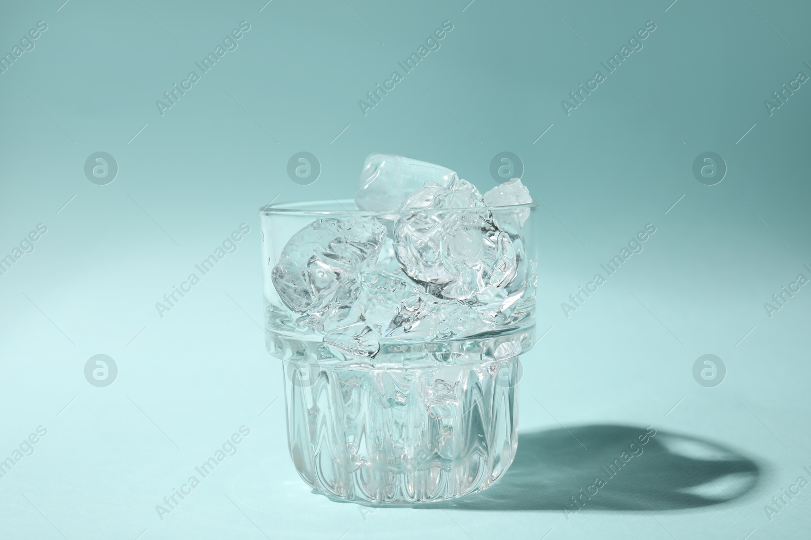 Photo of Refreshing water with ice in glass on turquoise background