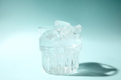 Photo of Refreshing water with ice in glass on turquoise background, closeup