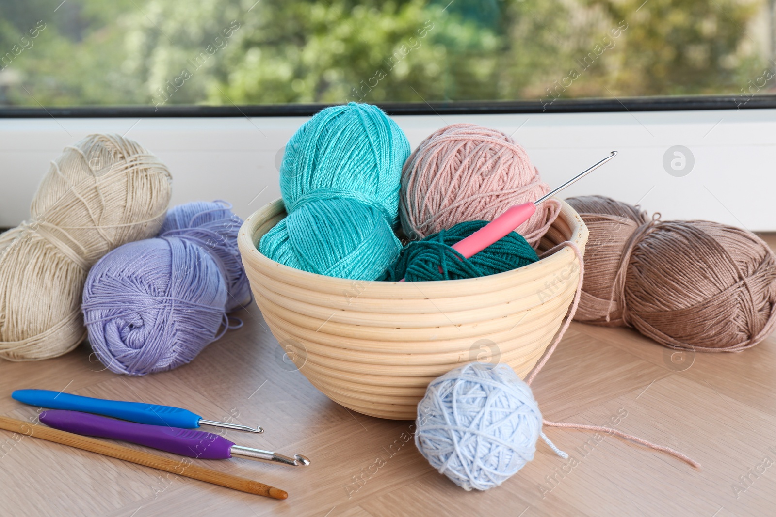 Photo of Different yarns and crochet hooks on wooden sill near window