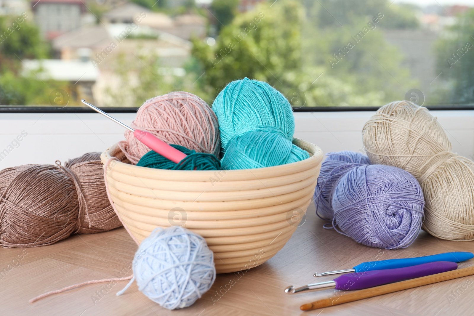 Photo of Different yarns and crochet hooks on wooden sill near window