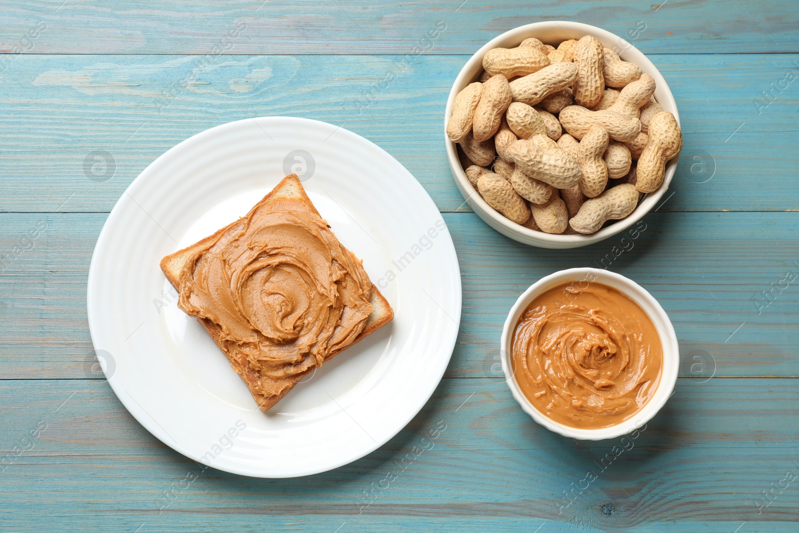 Photo of Tasty sandwich with peanut butter and nuts on light blue wooden table, flat lay