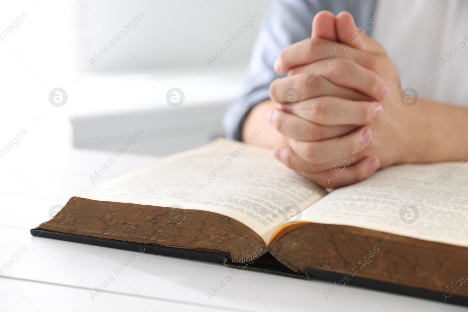 Photo of Man with Bible praying at white wooden table, closeup