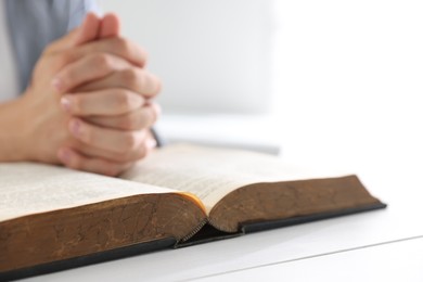 Photo of Man with Bible praying at white wooden table, closeup