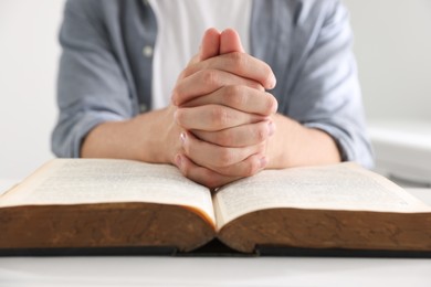 Photo of Man with Bible praying at white wooden table, closeup