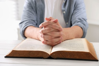 Photo of Man with Bible praying at white wooden table, closeup