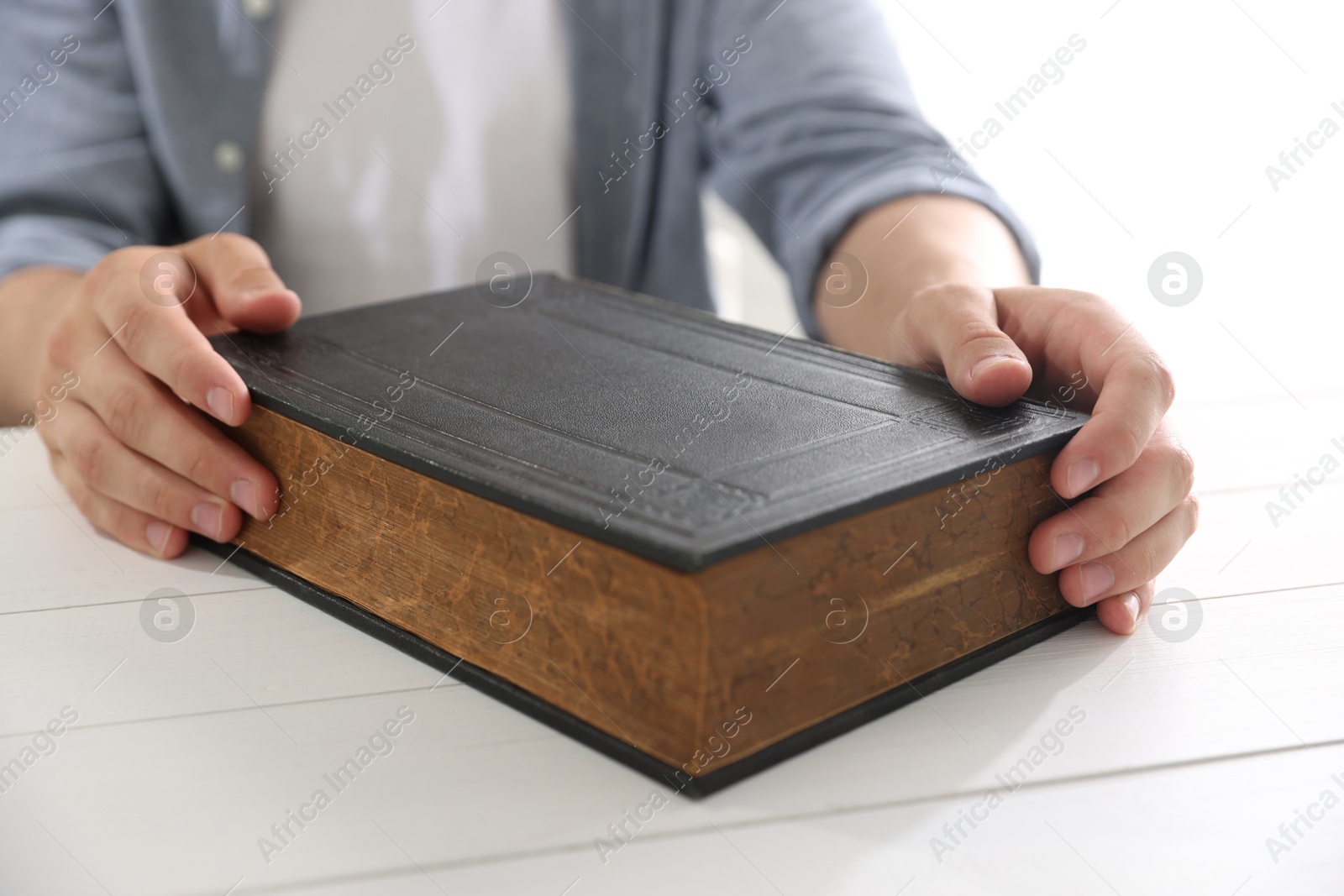 Photo of Man with Bible at white wooden table, closeup