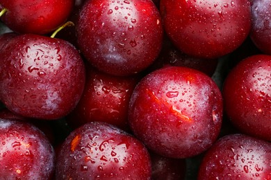 Photo of Many fresh plums with water drops as background, top view