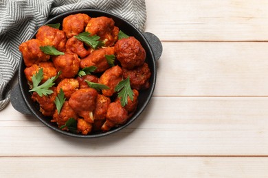 Photo of Baked cauliflower buffalo wings with parsley in baking dish on wooden table, top view. Space for text