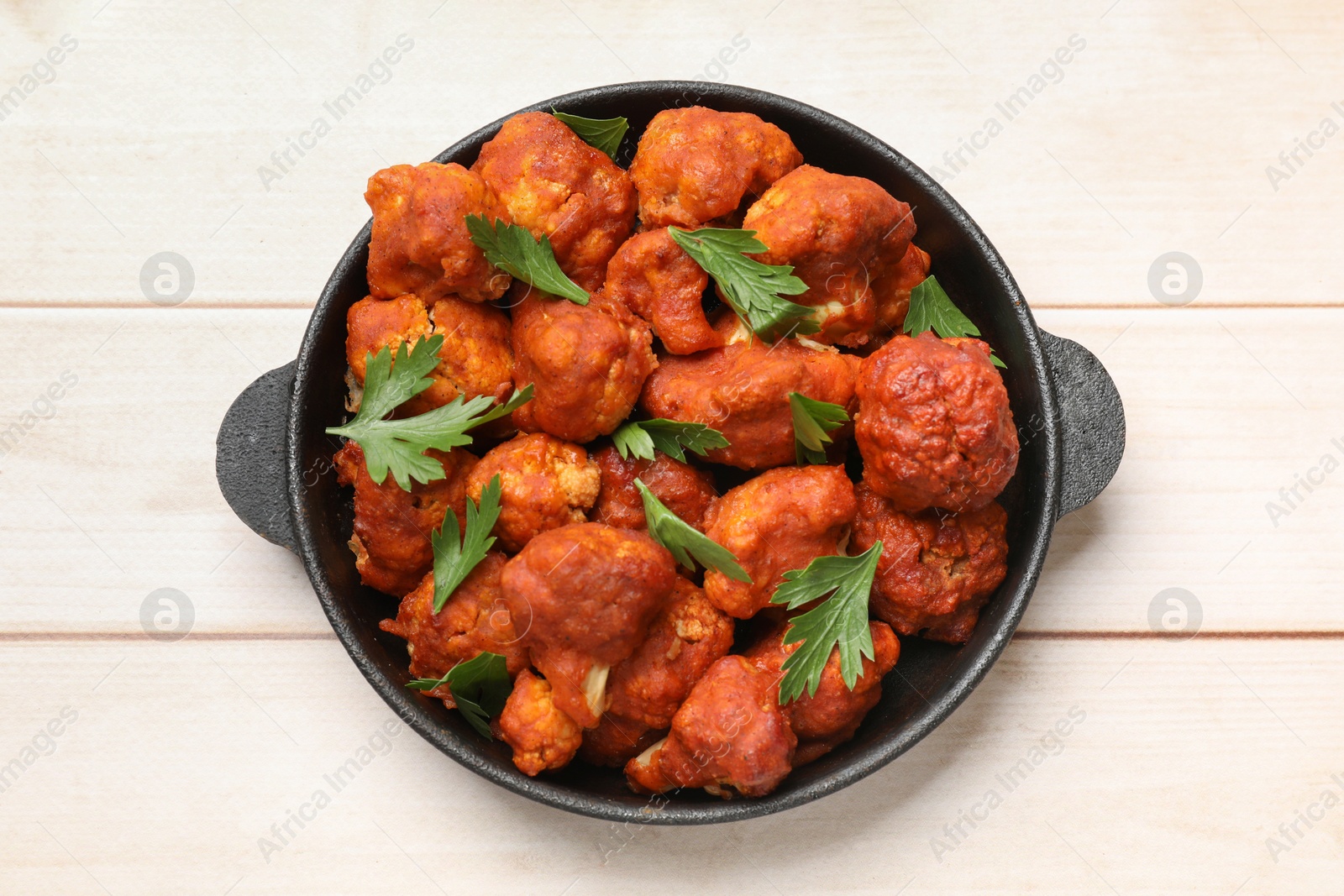 Photo of Baked cauliflower buffalo wings with parsley in baking dish on wooden table, top view