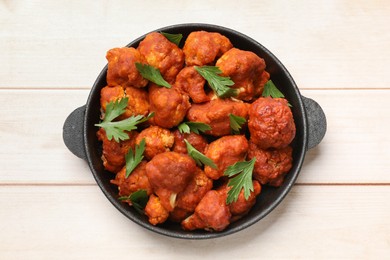 Photo of Baked cauliflower buffalo wings with parsley in baking dish on wooden table, top view