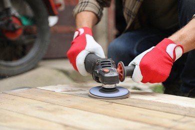 Man polishing wooden planks with angle grinder outdoors, closeup