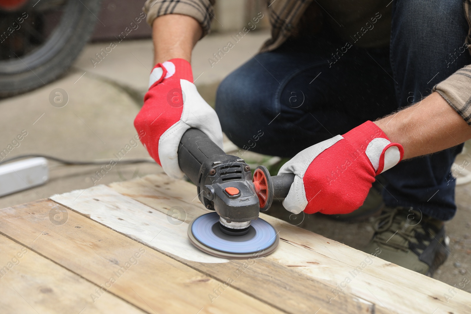 Photo of Man polishing wooden planks with angle grinder outdoors, closeup