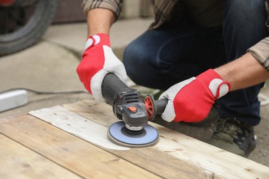 Man polishing wooden planks with angle grinder outdoors, closeup