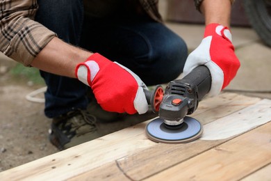 Photo of Man polishing wooden planks with angle grinder outdoors, closeup