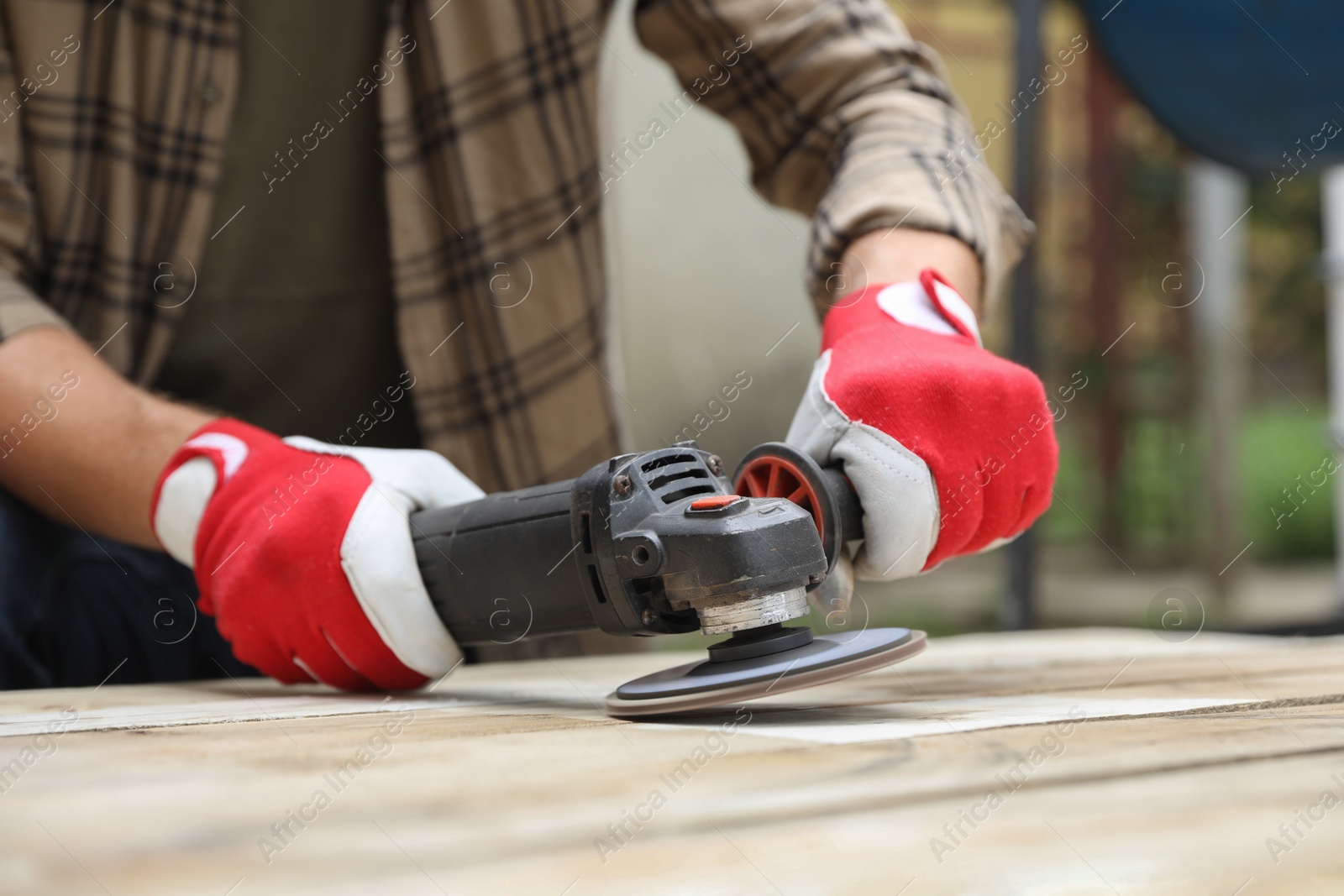 Photo of Man polishing wooden planks with angle grinder outdoors, closeup