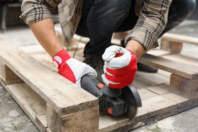 Man grinding wooden planks with angle grinder outdoors, closeup