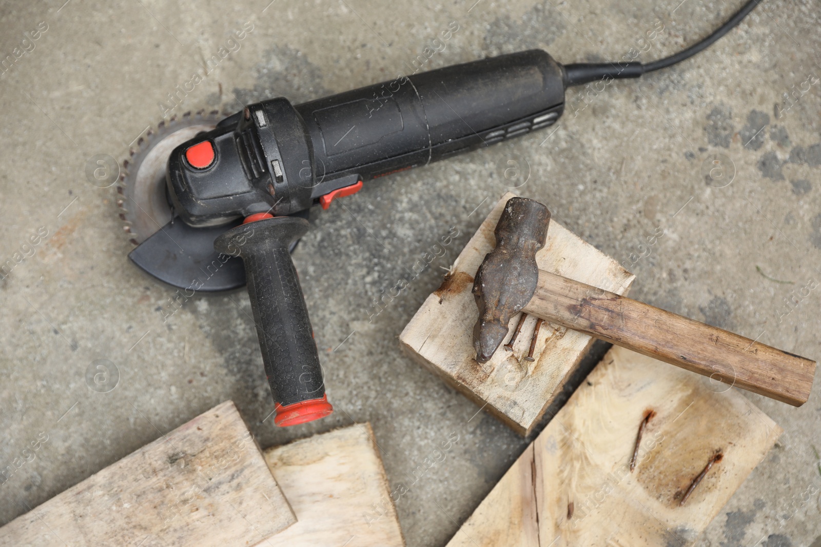 Photo of Angle grinder, hammer and wooden planks on asphalt outdoors, top view