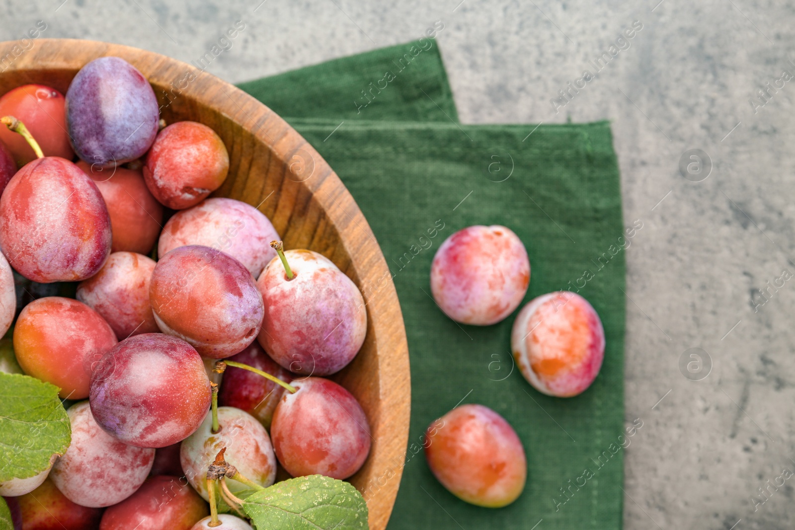 Photo of Ripe plums in bowl on grey textured table, flat lay