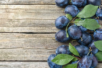 Photo of Tasty ripe plums and leaves on wooden table, flat lay. Space for text