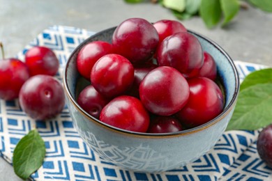 Photo of Tasty ripe plums in bowl on grey table, closeup